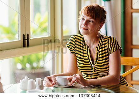 Girl sits in cafe and looks at him holding a Cup of tea in hand. The morning Breakfast