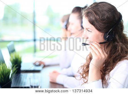Portrait of smiling female customer service agent wearing headset with colleagues working in background at office