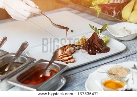 Liquid pouring on cooked meat. Hand holding spoon over plate. Duck steak prepared by chef. Delicious sauce for poultry meat.