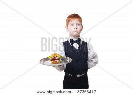 Little waiter stands with tray serving hamburger. Redhead child boy in suit plays restaurant servant, gives burger isolated at white background