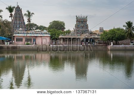 Tamil Nadu India - October 18 2013: Pillayarpatti Karpaga Vinayagar temple seen from the other side of the temple pond. Gray-blue sky green trees envelope the Gopurams and entrance buildings.
