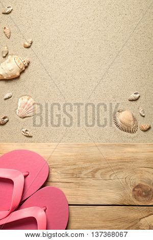 Summer concept with pink flip flops and shells on sandy beach. Top view
