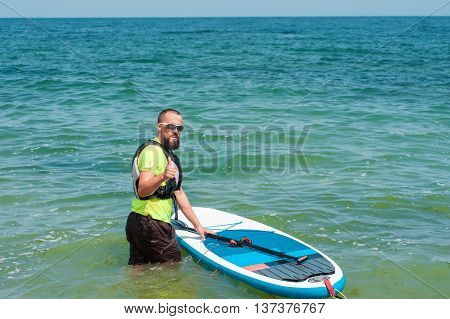young bearded man with an oar preparing floats on a paddle board in the sea it shows thumb