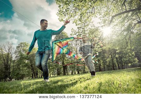 Runnings little boy and father flies with them kite in the park under sunligt.
