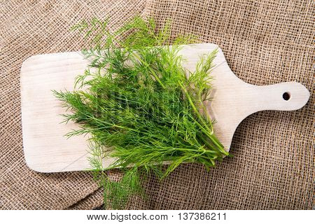Fresh green dill on wooden cutting board on jute bag