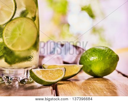 Alcohol drink. On wooden boards is part of glass with alcohol drink and ice cubes. Drink number thirty nine cocktail mohito and scoop ice and quartered lime. Country life cocktail . Light background.