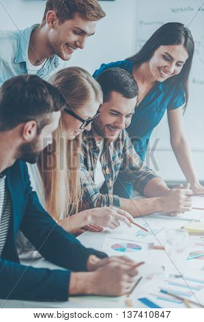 Business team at work. Side view of five cheerful business people in smart casual wear discussing something while looking at the graphs and charts