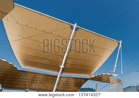 Detail of a modern tensile structure membrane fabric roof with poles and steel cables on a blue clear sky