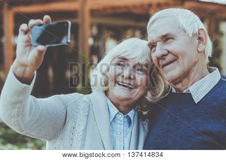 Capturing real love. Happy senior couple bonding to each other and making selfie while standing outdoors