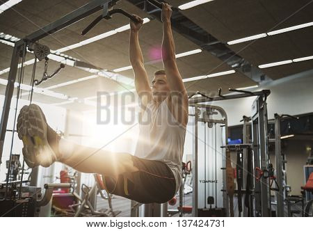 sport, fitness, lifestyle and people concept - young man flexing abdominal muscles on pull-up bar in gym