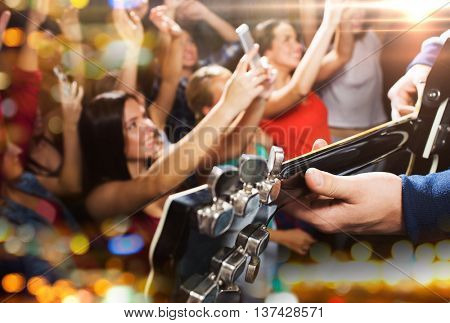 holidays, music, nightlife and people concept - close up of musiciab playing electric guitar on stage over happy people crowd taking picture by smartphones and waving hands at concert in night club