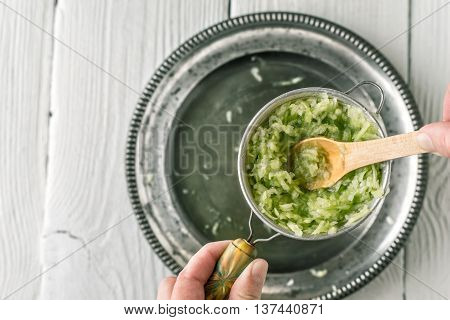 Grated cucumbers in the strainer with wooden spoon top view