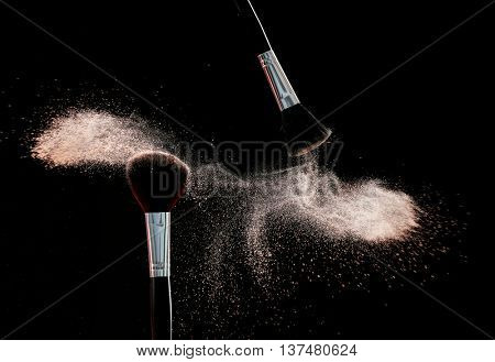 Makeup brushes with flying powder on black background