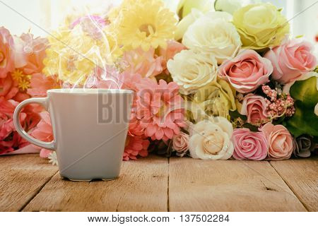 Cup of hot coffee on a wooden table with flower background under morning sunlight.Toned image.