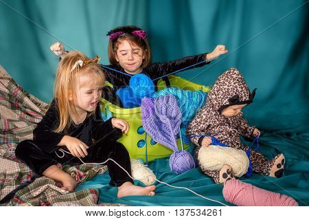 Three young girls dressed up in cat costumes play with yarn and knitting projects.