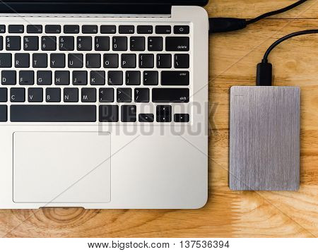 Top view of external or portable hard drive (HDD) connected to laptop computer for transfer or backup data on wooden texture office desktop