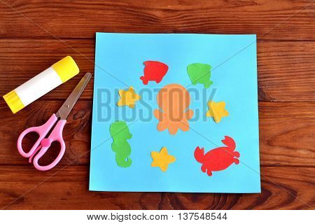 Paper card with sea animals and fishes. Creative ocean creatures crafts for kids. Paper octopus, fish, starfish, seahorse, crab project for children. Scissors, glue on a wooden table