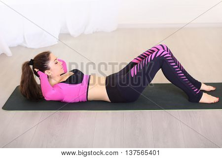 slim and sporty woman workout on the mat in bright room. She doing abs. Dressed in colorful sportswear.