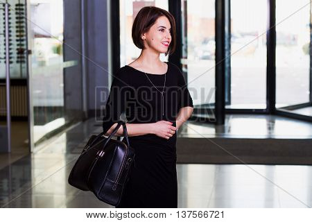 handsome and beautiful young businesswoman in black dress walking with briefcase in shopping mall. looking and smiling