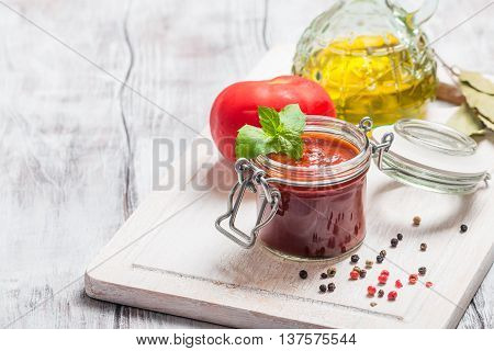 Glass jar with homemade classic spicy tomato pasta or pizza sauce. Italian healthy food on white wooden background.