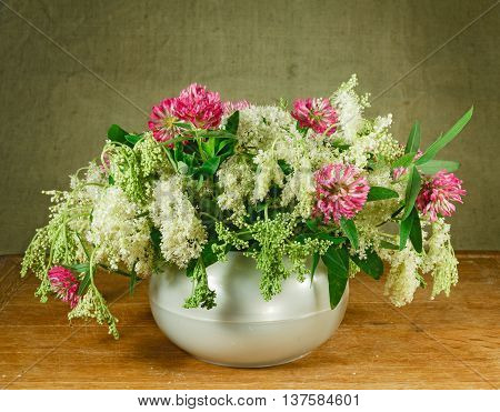 Alfalfa meadowsweet. Still life. Bouquet of meadow flowers in white pots standing on a wooden table. Rustic style.