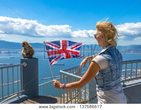Tourist woman holding an English flag observes one of the famous monkeys of Gibraltar from the top of Gibraltar Rock, in the Upper Rock Natural Reserve.