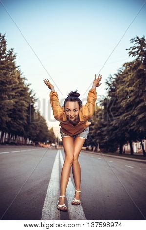 A young girl stands in a pose going to run or jump. The girl looks into the camera. Hands pulled back.