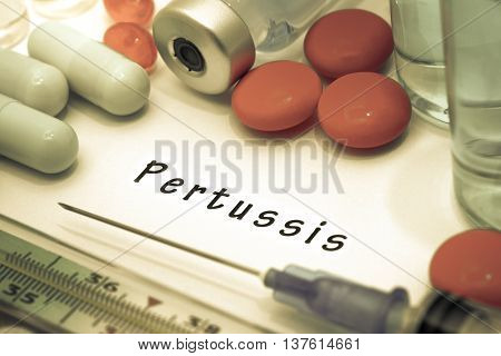 Pertussis - diagnosis written on a white piece of paper. Syringe and vaccine with drugs.