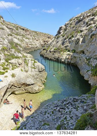 Wied il-Ghasri, Malta - September 26, 2013. The narrow cliff-bound inlet of Wied il-Ghasri with a tiny shingle beach and people.