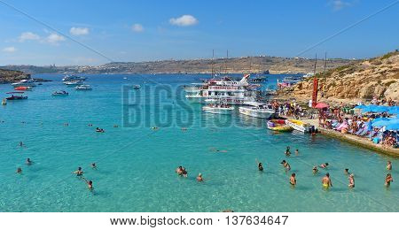 Comino, Malta - September 28, 2013. View of the Blue Lagoon on Comino island of Malta, with people, cruise boats and Gozo island in the background. The incredibly beautiful and inviting Blue Lagoon is the biggest attraction of Comino. It is a sheltered co