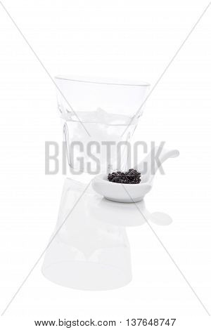 Delicious black caviar on spoon with vokda with ice isolated on white background. Exquisite luxurious gourmet eating.