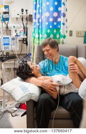 Caucasian father holding sick disabled son on lap in hospital. Child has cerebral palsy.