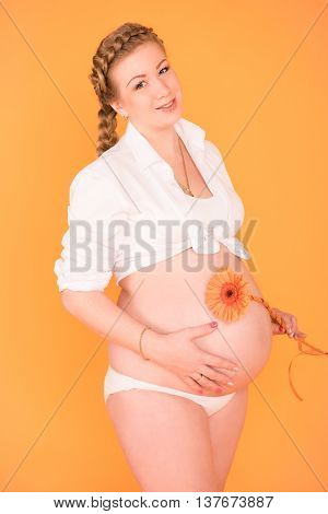 Pregnant woman with a flower in her hand on an orange background