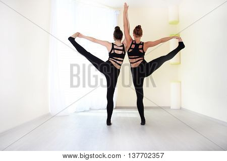 Athletes dressed in a stylish tracksuit standing on one leg and holding hands view from the back. Practicing yoga exercises