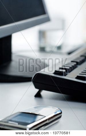 Imagen de teléfono acostado sobre una mesa con monitor, teclado y vidrio en él