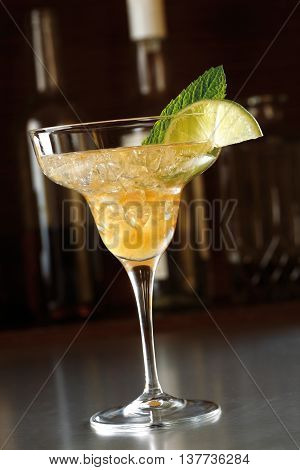 Refreshing cocktail in a high glass on the counter of a bar in dark ambience. Decorated with lime and mint.