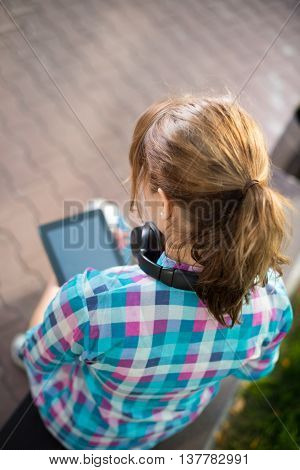Preparing to exams outdoors. Beautiful young female student writing or reading something from note pad.  Woman sitting on bench in city park.