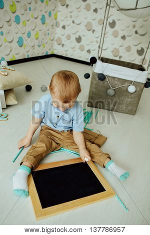 Attractive kid looking at blank chalkboard indoors. Kid having fun at home. Boy in bowtie looking away. Blank chalkboard.