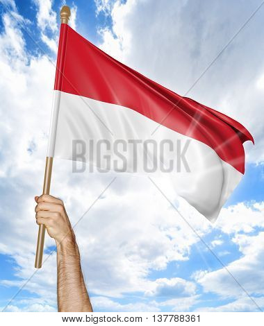 Person's hand holding the Indonesian national flag and waving it in the sky, 3D rendering