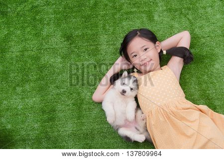 Cute asian girl lying with her puppy on green grass
