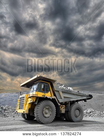 Heavy mining truck driving through the iron ore opencast with dramatic sky on the background