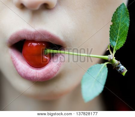 Red cherry in sensual open mouth with rosy lips on young woman face