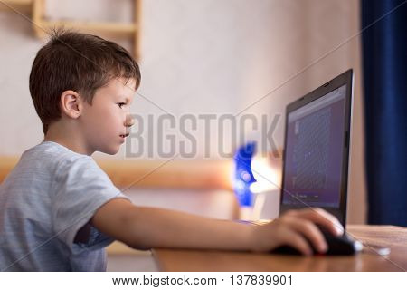Little dependent boy playing game on laptop at home