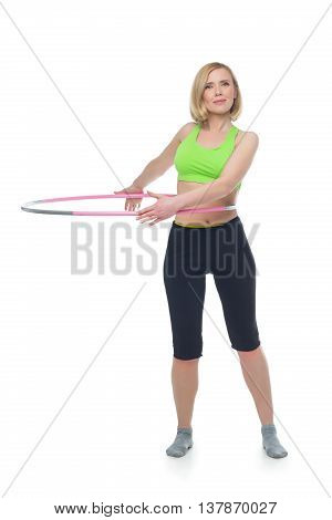 Beautiful middle aged blond fit woman in green bra top and black pants doing sport exercise with hula hoop. Isolated over white background. Copy space.