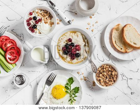 Assortment of breakfast - oatmeal with berries fried egg fresh vegetables cottage cheese yogurt and berries homemade granola on a light table. Healthy food. Top view