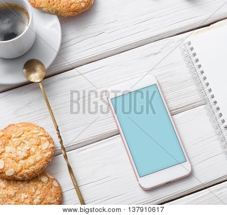 Mock up of white smart phone on a cafe desktop among cookies with coffee cup. Clipping path included.
