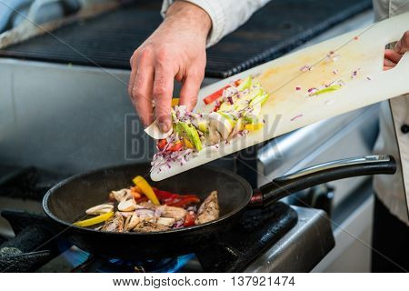 Chef putting ingredients to pan on cooker in restaurant kitchen