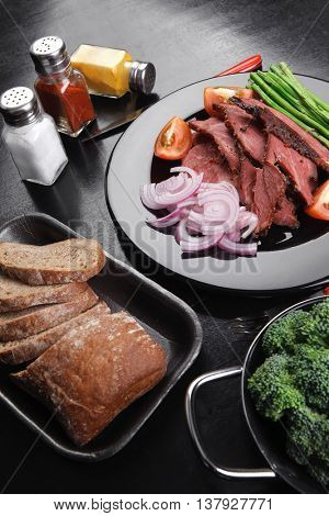 business lunch fresh roast beef meat slices on black plate wotj cutlery asparagus boiled broccoli rye bun on wooden table