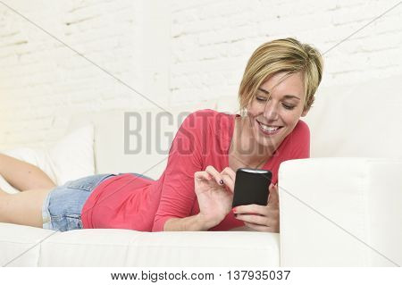 young beautiful Caucasian woman with shorts and modern hair style happy on couch using internet texting on mobile phone relaxed and cheerful at home living room in communication concept