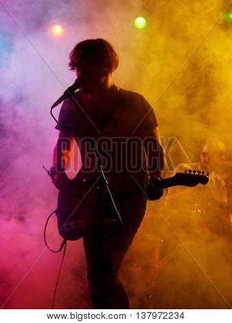 Silhouette of guitar player on stage. Dark background, smoke, spotlights